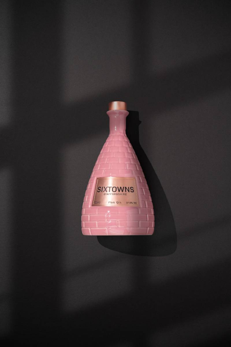 SIXTOWNS Pink Gin ceramic bottle placed on a dark background with dramatic window shadow lighting.