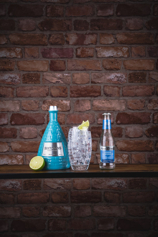 SIXTOWNS Alcohol-Free Spirit bottle served with premium tonic, highball glass, and fresh lime wedge, styled in front of rustic brick wall