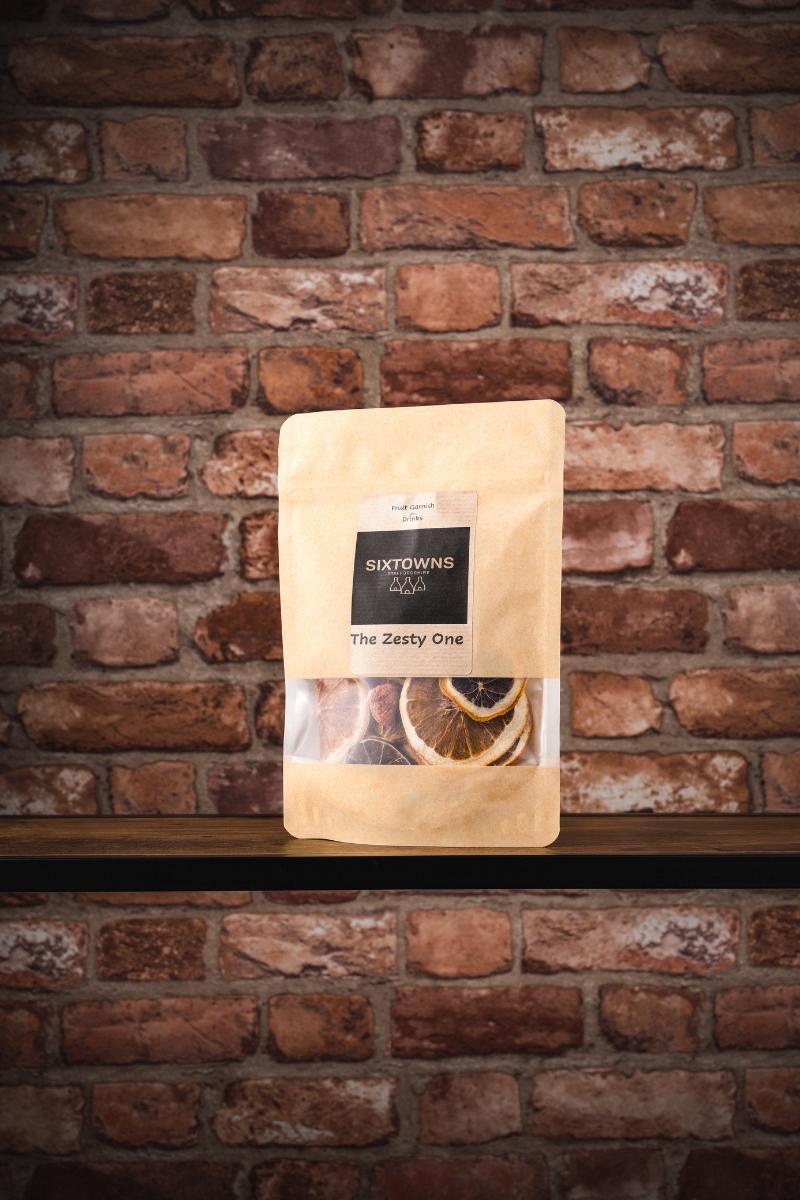 SIXTOWNS dried fruit garnish pouch labelled ‘The Zesty One’, displayed against a rustic brick wall background”